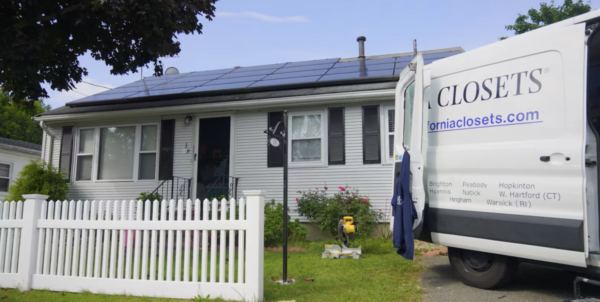 A white house with solar panels on the roof and a white picket fence. A van with "Custom Closets" branding is parked in the driveway.